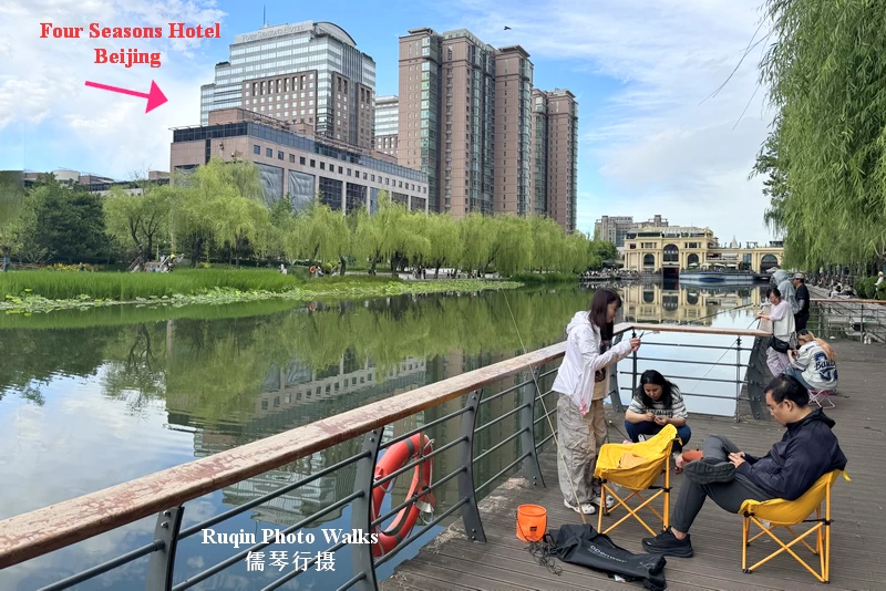 Four Seasons Hotel Beijing in the background, with people fishing along the riverbank of Liangma River