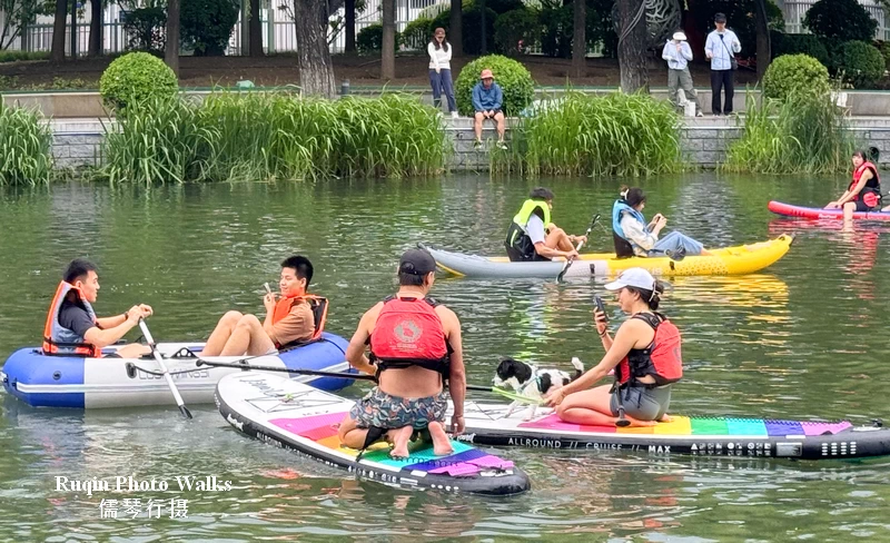 Kayaks, paddle boards, inflatable boats — and a dog riding a paddle board viewed from our Riverside Walk from Liangma River to Solana in Chaoyang
